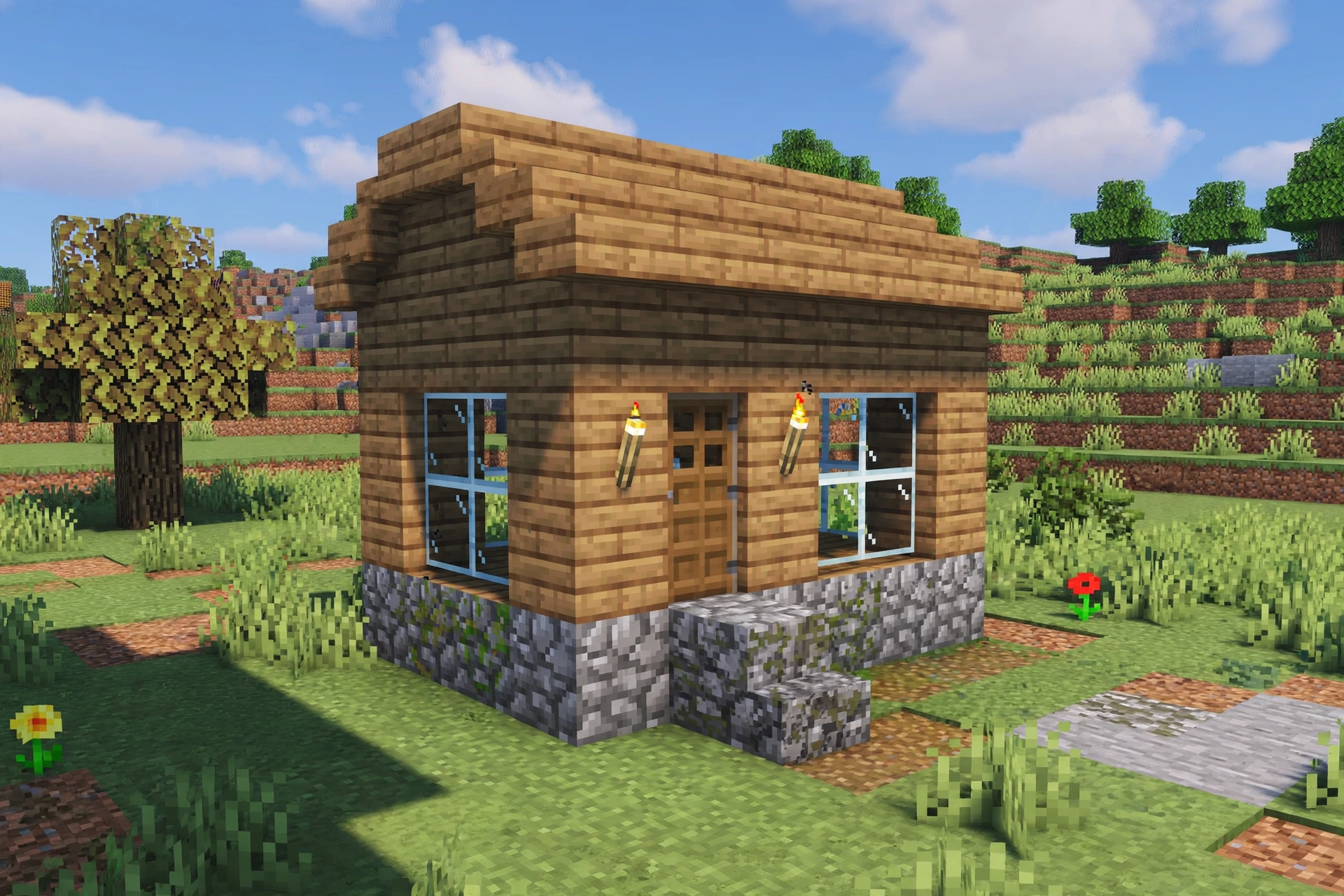 A Minecraft house with wooden plank walls, cobblestone foundation, glass windows and torches.