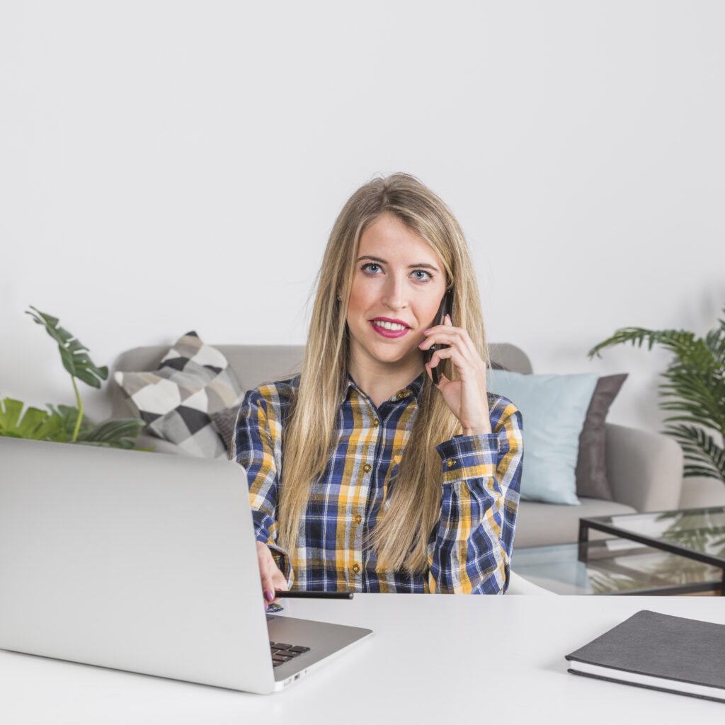 woman talking phone while sitting table with laptop